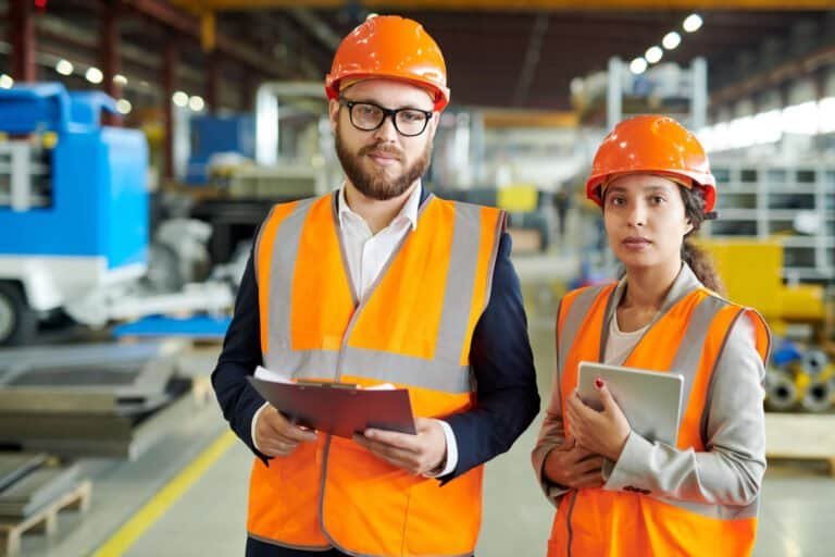 High-visibility construction workers inspecting equipment in a manufacturing plant.