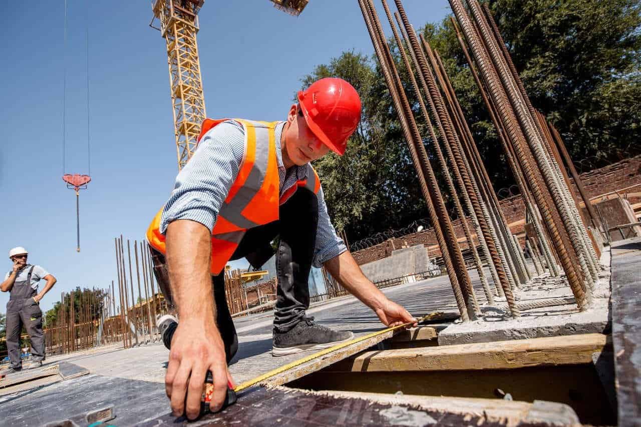 Construction worker measuring concrete formwork at a building site.