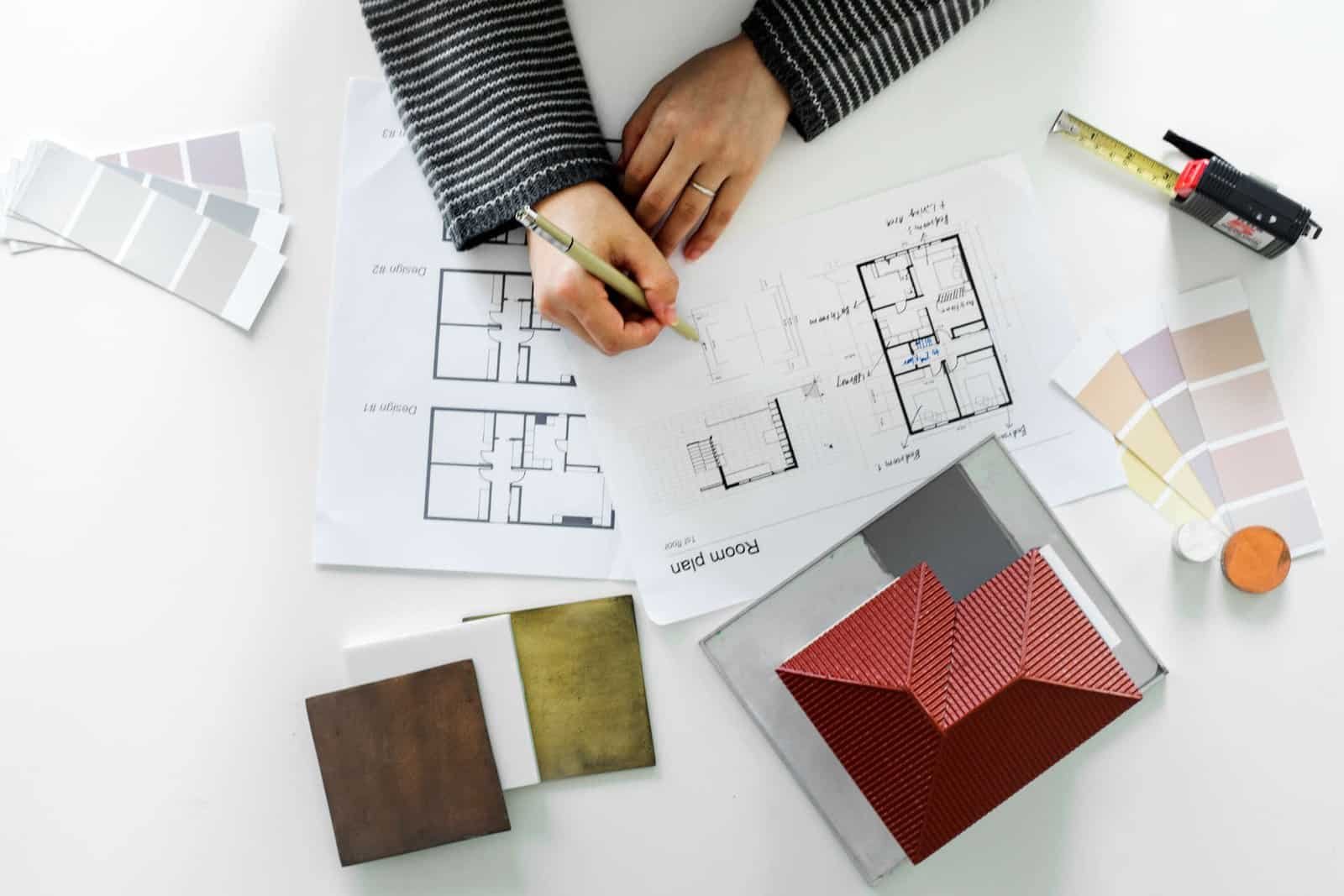 Architect reviewing building plans with color swatches and model house on white desk.