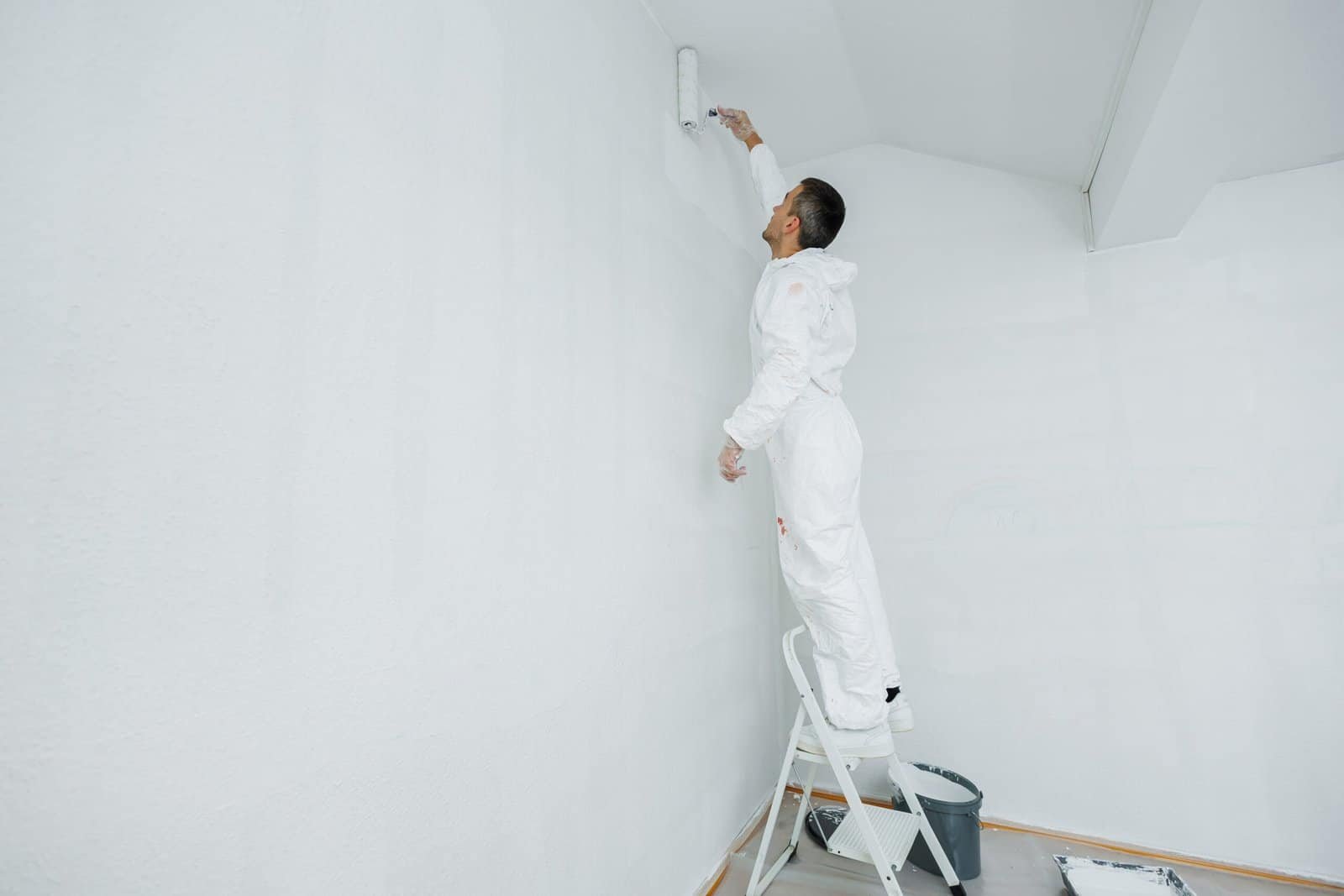 Painted wall with a person on a ladder applying a fresh coat of white paint, showcasing interior pai.