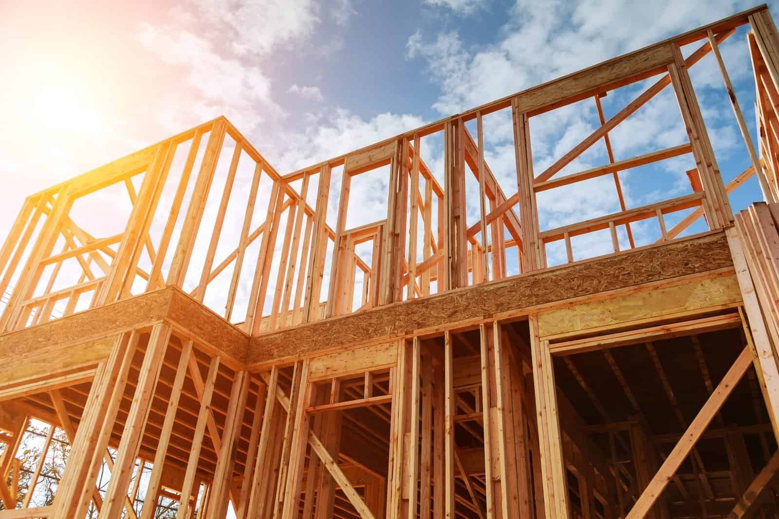 Wooden house frame under construction with blue sky and sunlight.