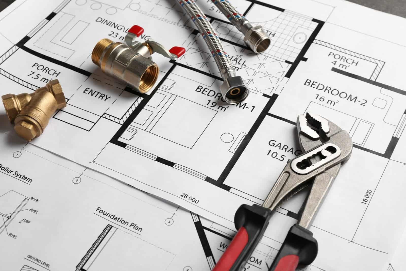 Brass plumbing fittings and adjustable wrench on architectural blueprint.