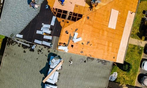 Residential roof construction in progress with workers installing new roofing materials.
